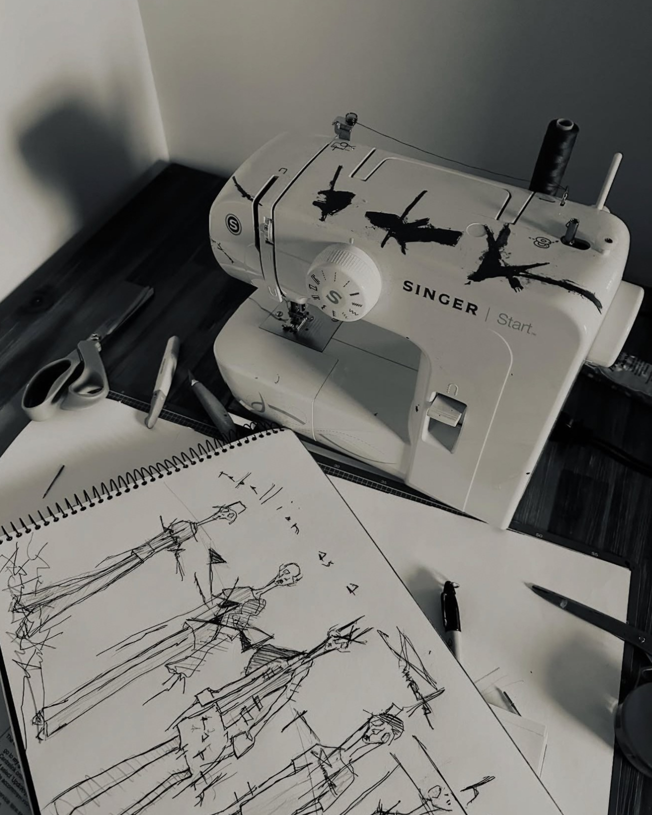 Jay_Jackal_s_sketchbook_with_biro_fashion_drawings_beside_a_hand-painted_sewing_machine_revealing_the_anonymous_artist_s_process