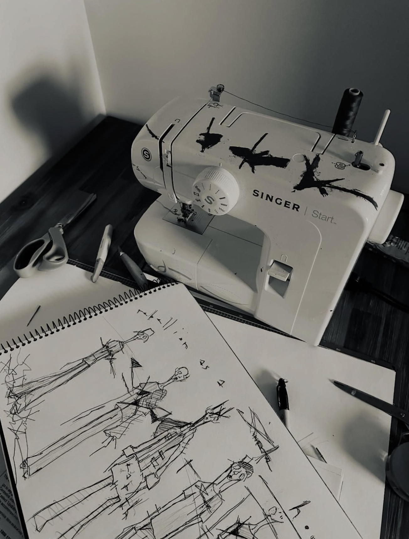 Jay_Jackal_s_sketchbook_with_biro_fashion_drawings_beside_a_hand-painted_sewing_machine_revealing_the_anonymous_artist_s_process