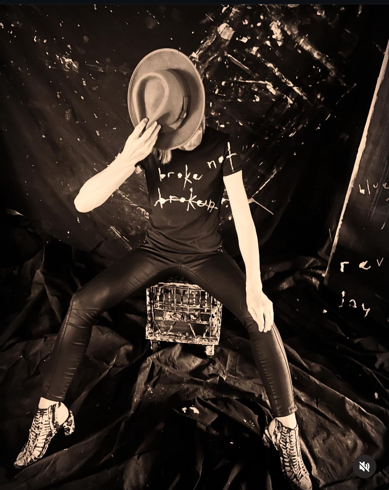 Jay Jackal wears a broke not broken hand painted t-shirt holding a hat to hide her face